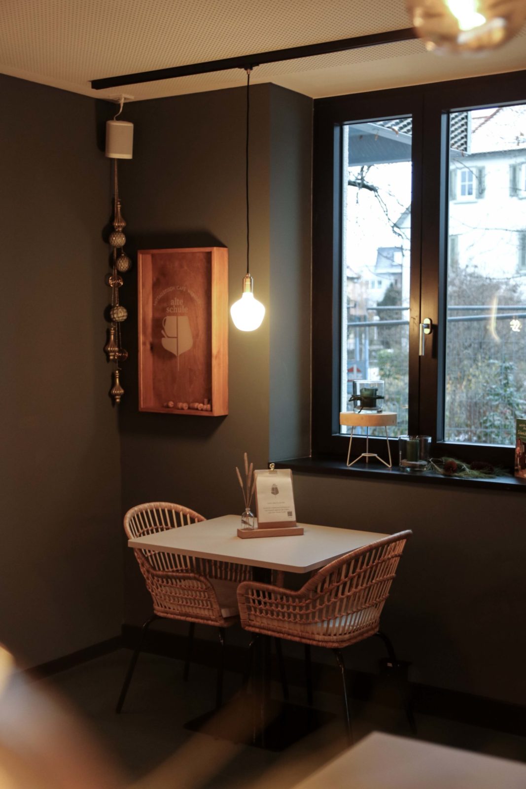 Innengestaltung Cafe, Bambussessel und Tisch an Fenster, warme Beleuchtung, weihnachtlich dekoriert